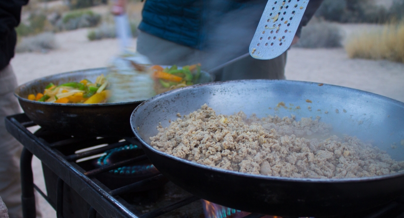 Two skillets of food cook over an outdoor stove